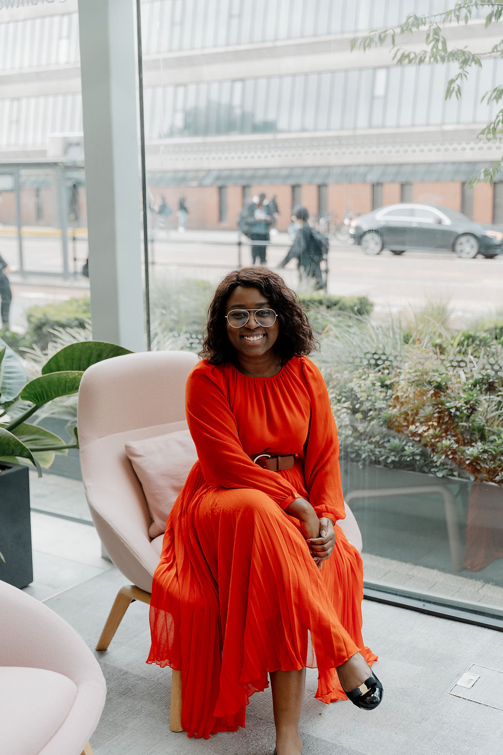 Lisa Maynard-Atem sitting by a window in a bright red dress, smiling confidently. A subtle overlay of green and pink shades frames the image, with the tagline “Progress it, or Park it. No maybes.” at the bottom.