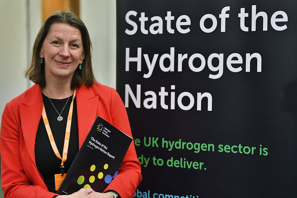 Dr Emma Guthrie, CEO of the Hydrogen Energy Association, standing in front of a large “State of the Hydrogen Nation” display while holding a copy of the Hydrogen Energy Association’s report. She is wearing a bright red blazer and smiling at the camera during an industry event focused on the future of hydrogen and the UK’s energy transition.