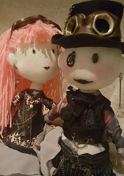 Two steampunk handmade reagdolls. one female with pink wool hair and other male with black hat.