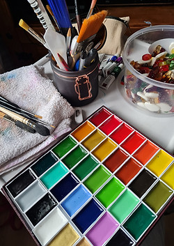 Pallete of watercolour paints with brushes and cloth. To the side of this jelly sweets.