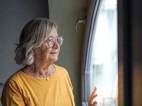 Older woman looking out a window during the evening while a family caregiver offers comfort, representing sundowning and the emotional changes associated with dementia.