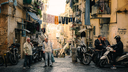 Men are chatting in the street, washing is stretched out on lines across the road to dry. 