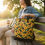 Thumbnail: Woman sitting on a park bench holding a sunflower bag AWESOMEROSE'S.