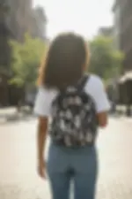 Thumbnail: Woman wearing backpack walking down city street. Small 3-section/adjustable strap bag.