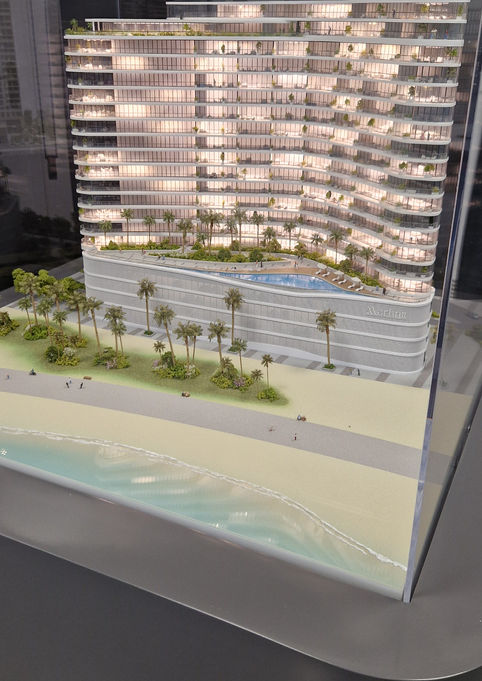 Maquette illuminée sous vitrine de la tour résidentielle de luxe "Marlin 2" à Abu Dhabi : architecture aux lignes ondulées évoquant les vagues, surplombant une piscine à débordement sur podium et une plage de sable fin bordée de palmiers et d'eau turquoise.
