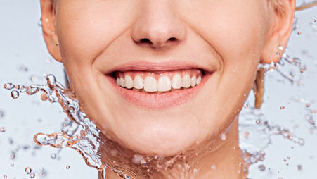 Woman with radiant skin smiling as water splashes around her face, representing deep hydration and natural glow after skin booster treatments at Luminous Skin in Nelson.