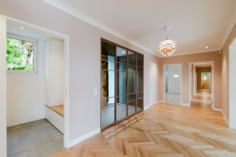 Innenaufnahme einer sanierten Villa mit hellem Fischgrätparkett, Glaswand und warmen Wandfarben, Querformat, hochwertige Architektur-Fotografie.