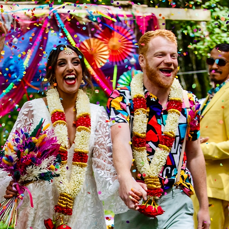 A happy couple dressed in bright colours walking down the aisle on their wedding day