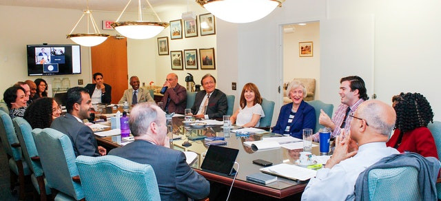 an image of people sitting down and discussing and taking notes around a long rectangular table are shown