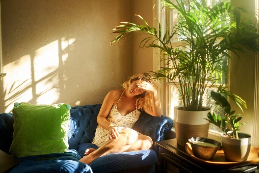 Woman sitting quietly in warm sunlight surrounded by indoor plants during a peaceful moment of emotional reflection and self-care.