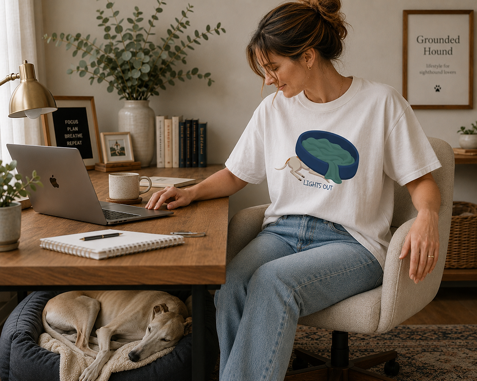 Woman working at her desk wearing "Lights Out" whippet and greyhound tee with a sleeping whippet under her desk.