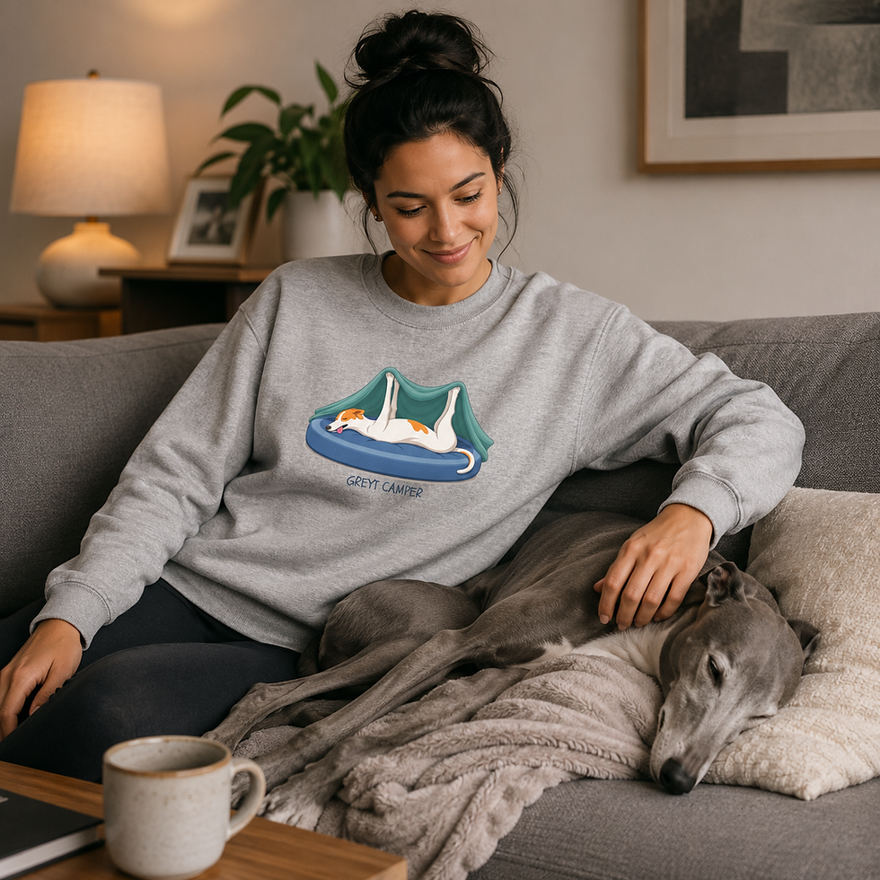 Thumbnail: Woman relaxing on a couch wearing the "Greyt Camper" sweatshirt with a sleeping greyhound next to her.