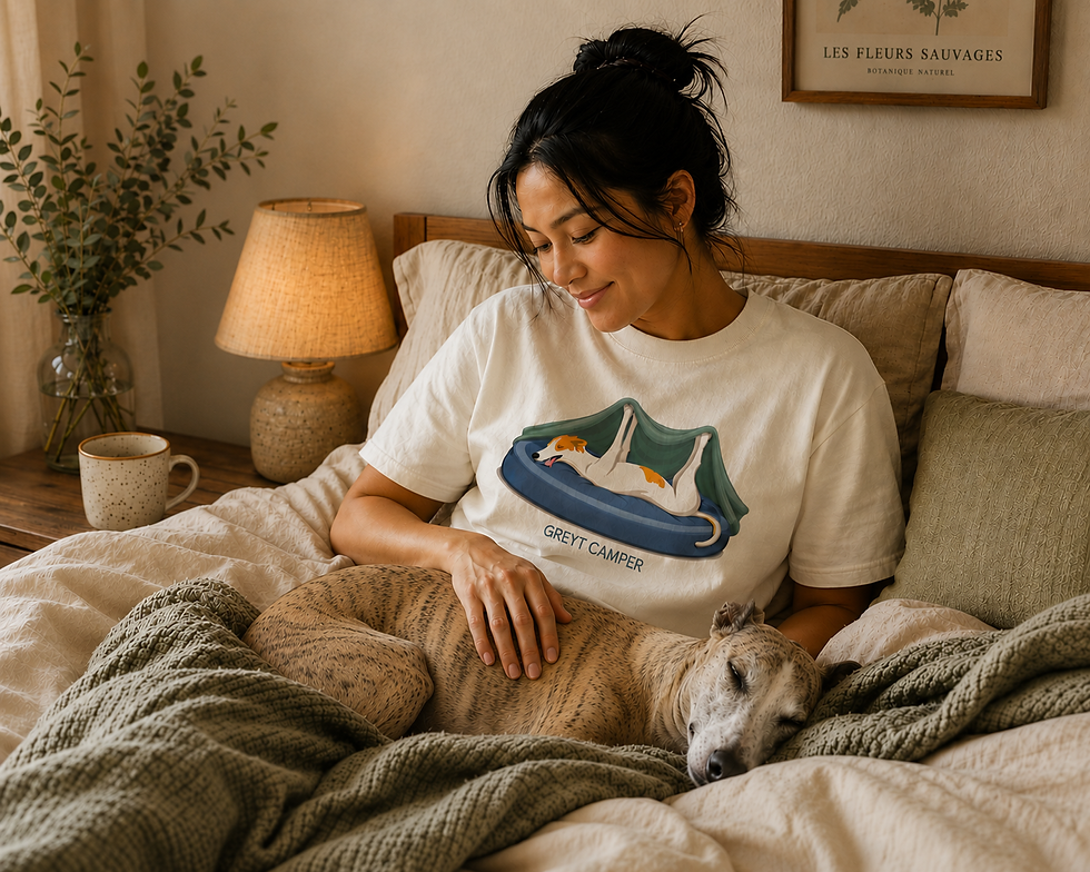Woman relaxing in bed wearing the "Greyt Camper" tee with her whippet sleeping on her lap.