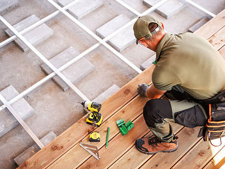 Worker installing wooden deck boards with tools.