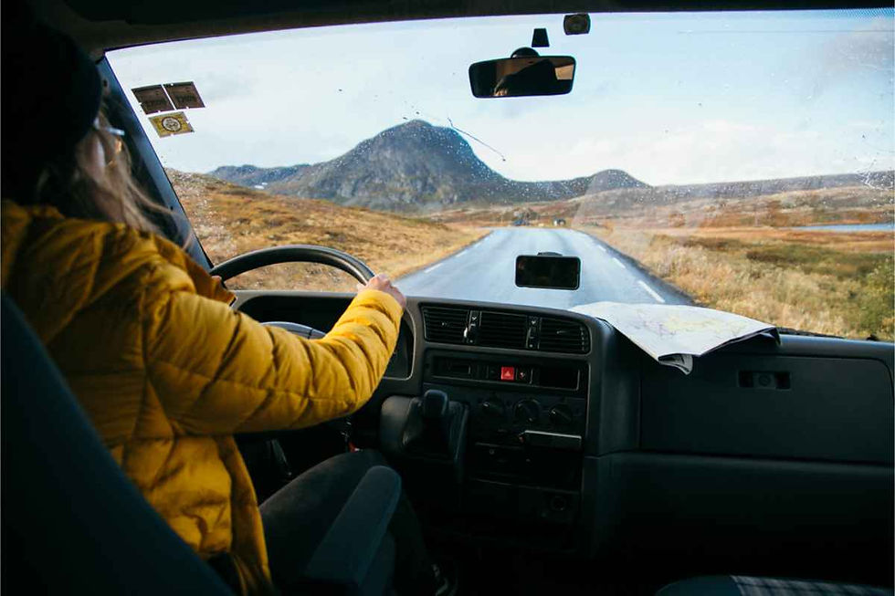 Person in a yellow jacket driving on a scenic road in Iceland with mountains ahead, map on the dashboard. Overcast sky sets a tranquil mood.
