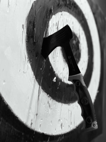 Close up of an axe buried in the bullseye of a wooden target during an indoor throwing session.