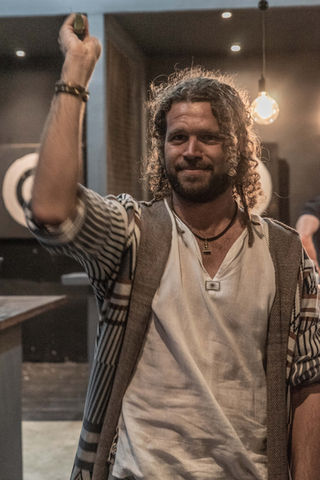 Smiling man with long curly hair holding an axe up during a social event at an indoor venue.