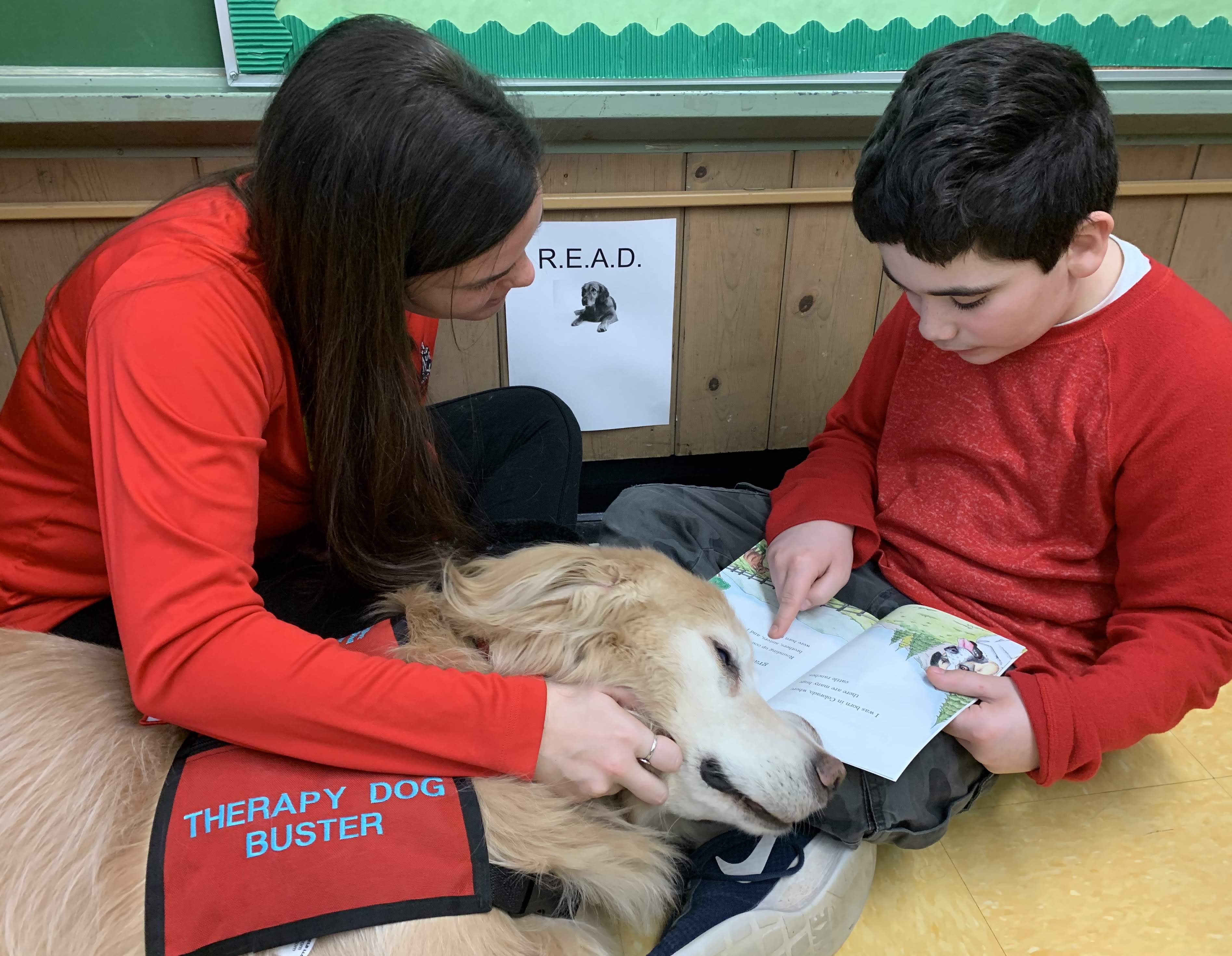 Christina and therapy dog Buster helping a child learn to read in R.E.A.D. program