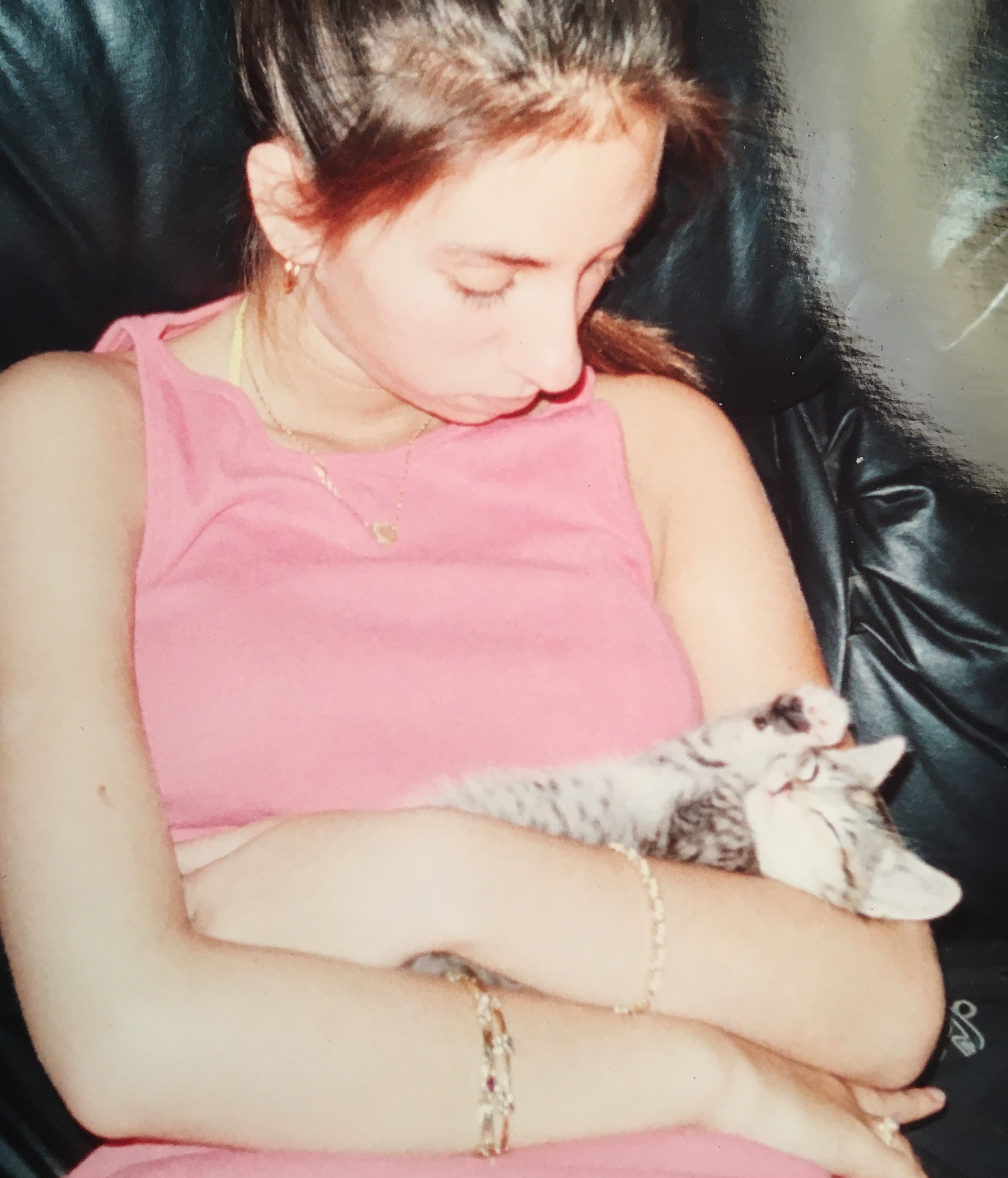 Paige Rechtman in a pink top cradles a sleeping gray-and-white kitten on a black chair, looking down softly