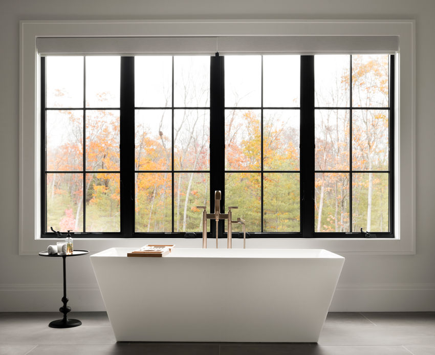 Interior design bathroom photoshoot featuring modern freestanding tub and black framed windows overlooking fall foliage in Mendon MA