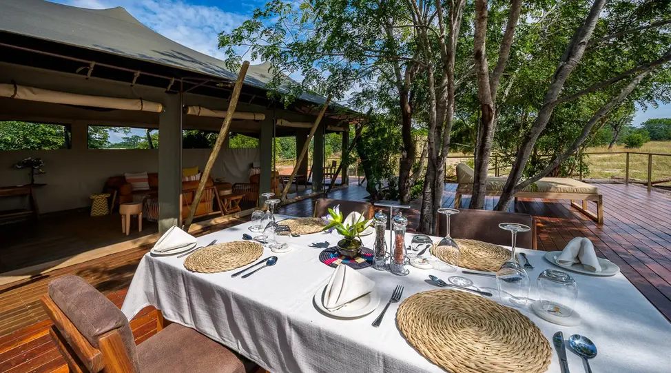 Outdoor wooden deck dining table beneath the trees at Muddy Teak Camp, ideal for relaxed meals during a Zimbabwe safari.