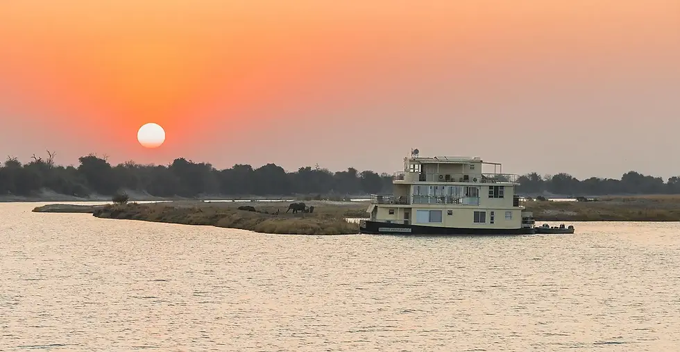 Chobe Princess houseboat cruising the Chobe River at sunset with elephants on the riverbank in the distance, luxury Botswana safari experience.