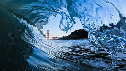 Featured image of Ring - an image of a glassy wave at sunrise with a gem-like piece of lip reaching down to frame the golden gate bridge in the image.