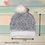 Thumbnail: Handmade crochet pom pom beanie fuzzy white and gray weave beanie, cozy winter hat for children. Shop Hugs in a Hat