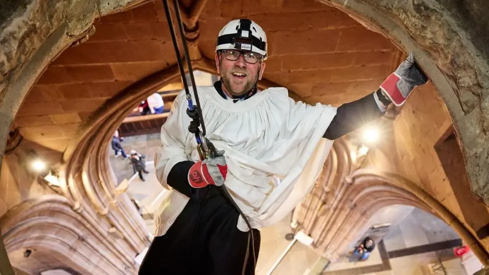 Rev Canon Phil Batchford waving as he abseils through Rotherham Minster