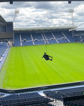 Man completing football stadium zip wire with his arms out to the sides