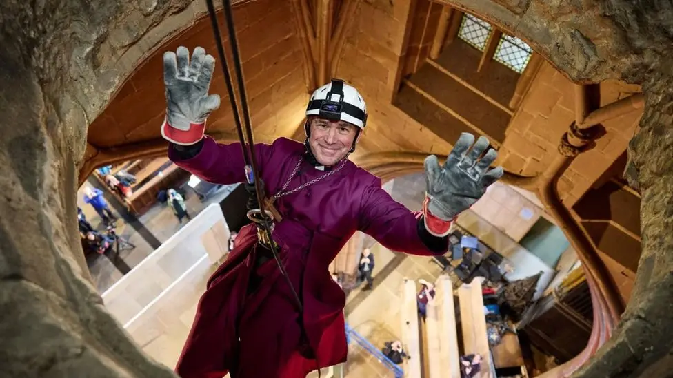 Rt Revd Dr Pete Wilcox waving whilst doing an abseil inside Rotherham Minster