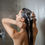 Thumbnail: A brunette woman rinses Tussah Silk & Aloe Vera Shampoo from her hair as steam rises in a hot shower.