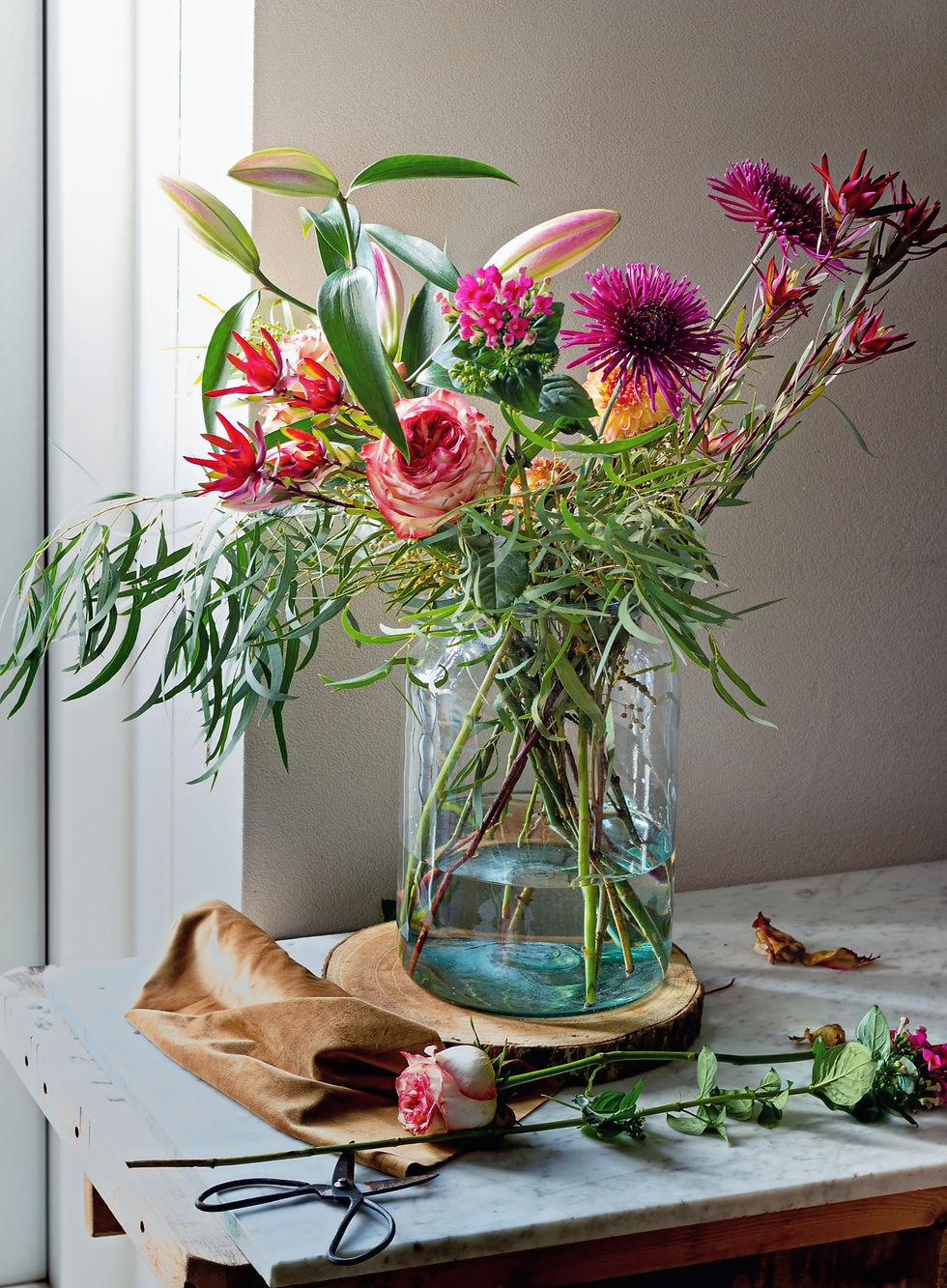 Eye-level view of fresh seasonal flowers in a clear vase on a kitchen bench.