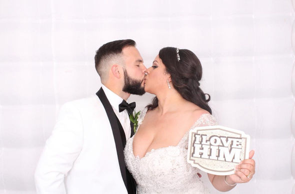 Bride and groom kissing with a "I Love Him" prop at a photo booth.