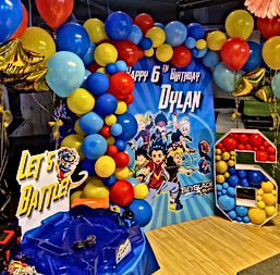 แบ็คดรอปสำหรับงานวันเกิดธีม "Beyblade" พร้อมตัวละครการ์ตูนและข้อความ "Happy 6th Birthday Dylan" ล้อมรอบด้วยลูกโป่งสีแดง น้ำเงิน และเหลือง มีป้าย "Let's Battle" อยู่ทางด้านซ้าย และสนามแข่งเบย์เบลดสีน้ำเงินอยู่ด้านหน้า ให้บรรยากาศสนุกสนานเหมาะสำหรับงานปาร์ตี้เด็ก : A colorful birthday party backdrop featuring a "Beyblade" theme with animated characters and the text "Happy 6th Birthday Dylan." The backdrop is surrounded by an arch of red, blue, and yellow balloons. A sign with "Let's Battle" is placed on the left, along with a blue Beyblade battle arena in the foreground, creating a lively and energetic party setting.