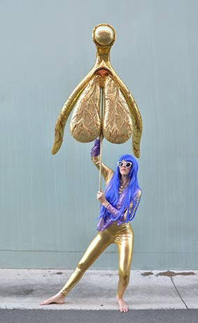 Artist Alli Sebastian Wolf in sunglasses stands holding a giant model clitoris (100:1 scale)