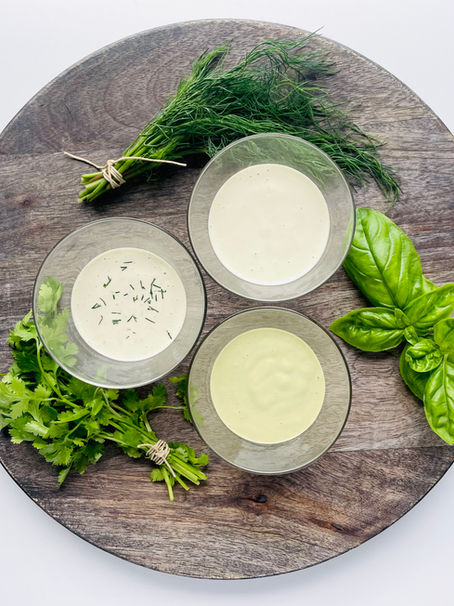Three bowls with creamy ranch dressing on platter with fresh herbs.