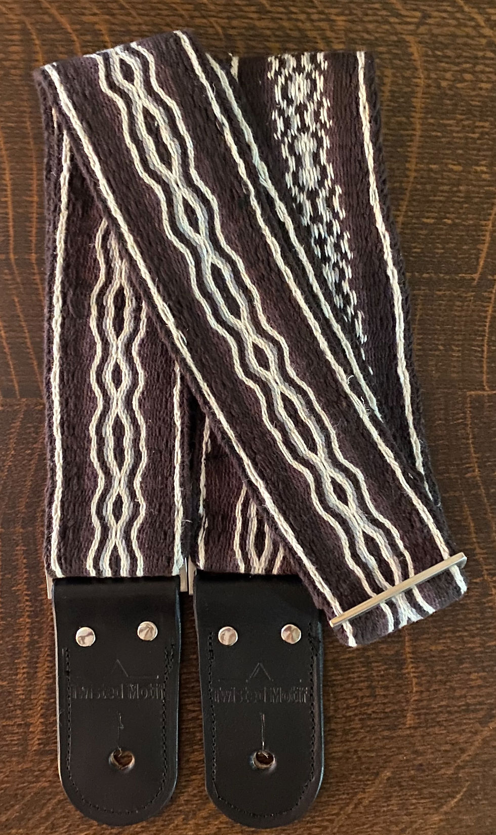 Close-up view of a handmade woven guitar strap laid flat on a wooden surface