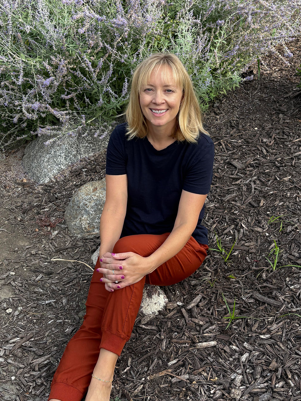 Portrait photo of the occupational therapist sitting outdoors in nature, wearing a black top and rust-colored pants, with soft natural colors and a landscape orientation.