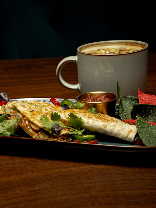 hicken quesadilla at Café Karak filled with chicken tikka, bell peppers, and melted cheese, served with a side of nachos.