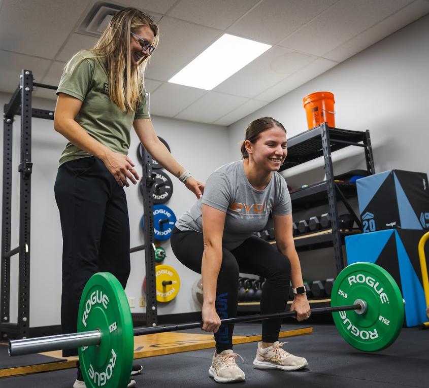 Therapist is working with a woman on corrective exercise. Woman is lifting barbell.
