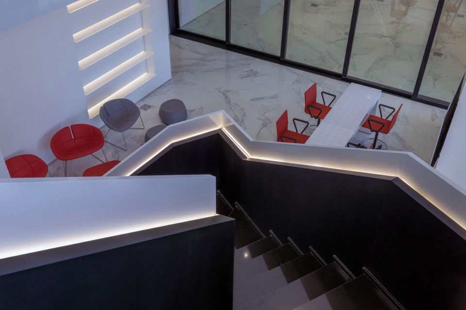 Modern office interior with red chairs, white table, and a staircase view.