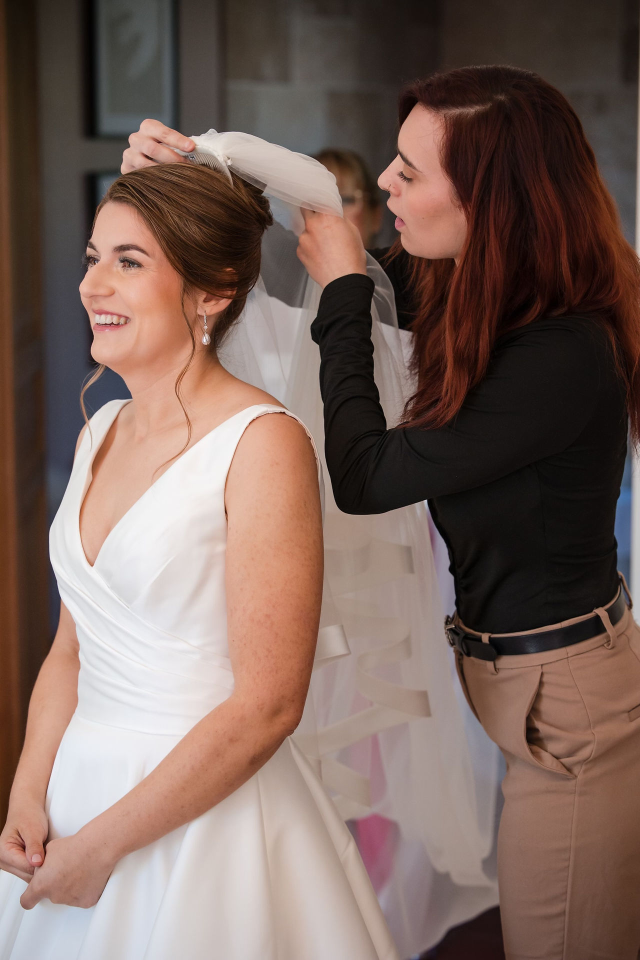 Coiffeuse qui pose le voile sur la coiffure d'une mariée qui est heureuse