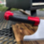 Red and black textured handle on wooden board next to an outdoor oven.