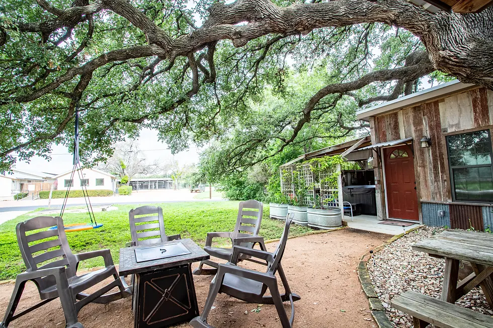 Fredericksburg rental homes: rustic cabin patio with fire pit seating under a mature oak tree