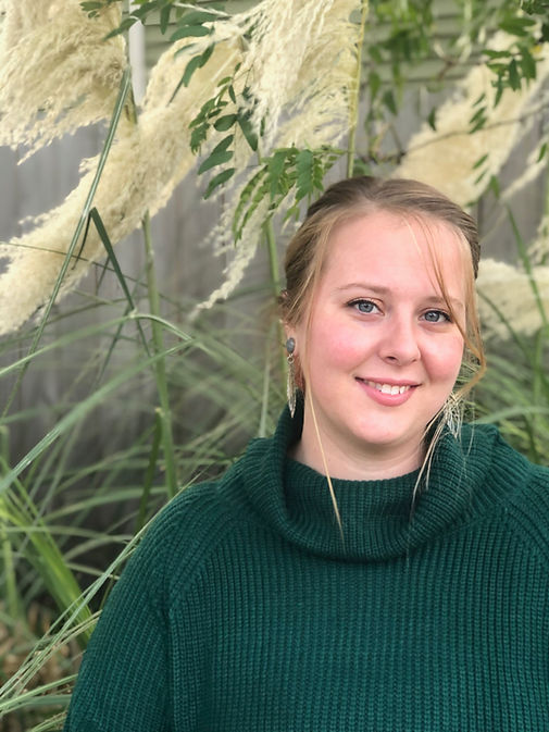 Therapist Haile Reeve in a green sweater smiling in front of tall grass.