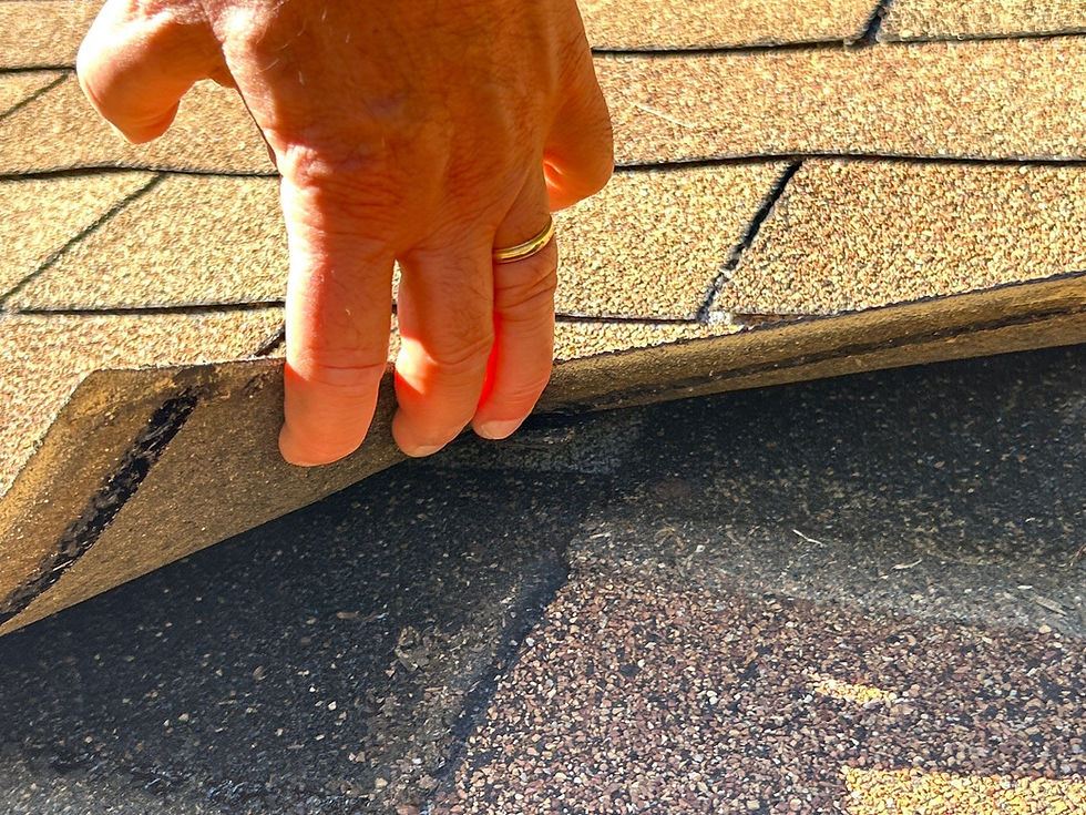 Hand inspecting roof shingles; brown roof visible. Roofing Contractor.