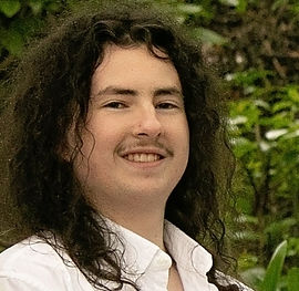 Smiling person with long curly hair and mustache