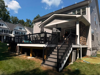 Elevated composite deck with black railing, wide stairs and gable covered porch on a gray home