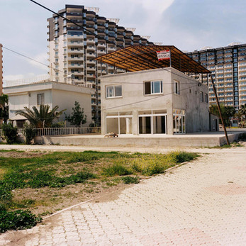 Unfinished two-story building FOR SALE surrounded by tall apartment blocks.